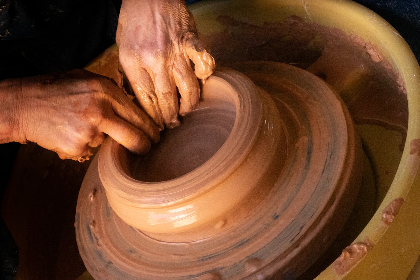 Clay-covered hands shaping a bowl on a pottery wheel
